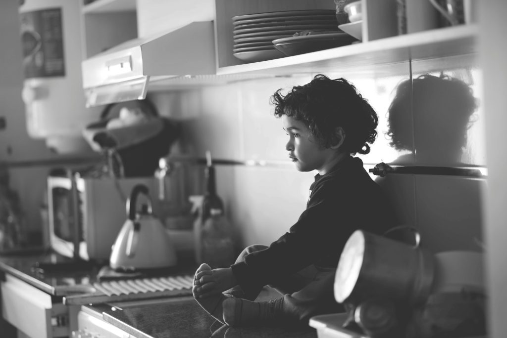 Young boy in a kitchen, reflecting in soft monochrome lighting.